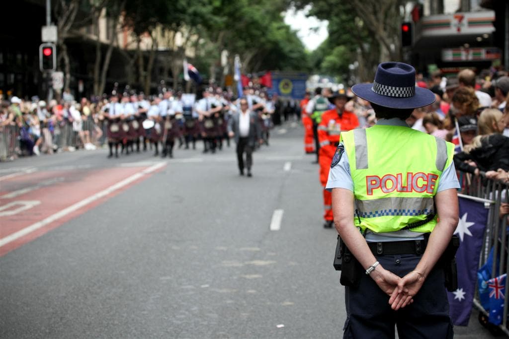 A police officer in a high-visibility vest watches a city parade.